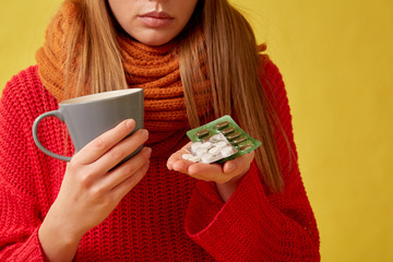 Sick girl holding pills and a cup in her hands. Image on yellow background.