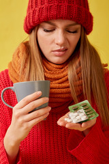 Sick girl holding pills and a cup in her hands. Image on yellow background.