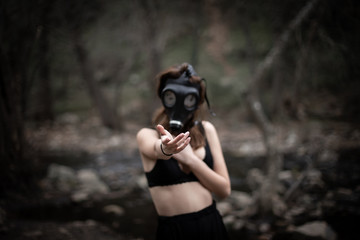 Anonymous woman in black clothes and gas mask standing in amazing spooky forest