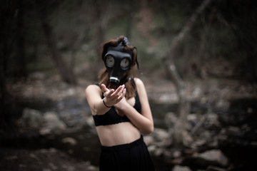 Anonymous woman in black clothes and gas mask standing in amazing spooky forest