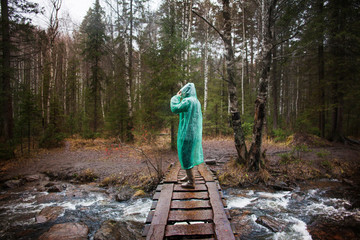 Woman in rain poncho standing on bridge over river 