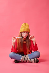 A sick girl in a yellow hat holds a medical thermometer and pills in her hands. Image on the pink background