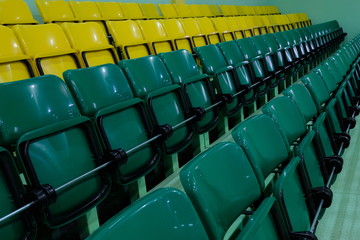 Plastic chairs for spectators in the gym. Auditorium with rows of raised green and yellow seats.