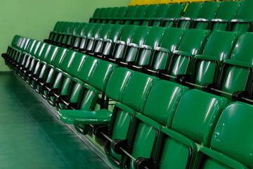 Obraz premium One seat is omitted for the viewer. Auditorium with rows of raised green seats. Plastic chairs for spectators in the gym.