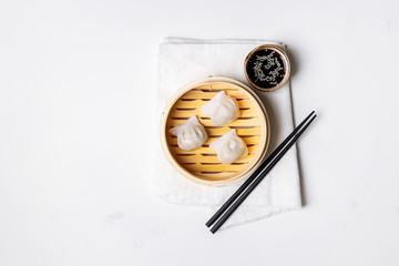 Traditional chinese steamed dumplings Dim Sums in bamboo steamer with sauces and chopsticks on light surface with copy space. Asian food background.