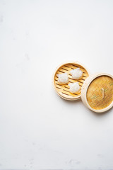 Traditional chinese steamed dumplings Dim Sums in bamboo steamer with sauces and chopsticks on light surface with copy space. Asian food background.