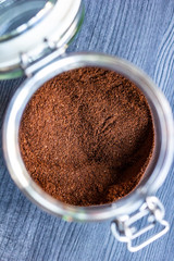 Ground aromatic, invigorating coffee in a transparent jar with an open lid and a metal lock on a wooden textured table.