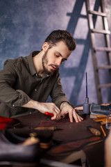 young active man cutting black leather with special knife in the room with blue wall and a ladder