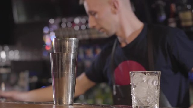 Handsome bartender mixologist using shaker and making an alcohol cocktail with different drinks in beautiful modern bar. Close up