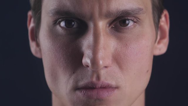 Close up portrait of young man opens his eyes and stares into camera on a black background