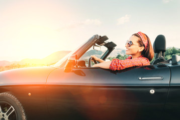Young cheerful smiling female  driving convertible car at sunny day time