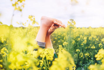 Legs up of happy female lying in deep yellow flowers meadow. Happiness in nature concept image.