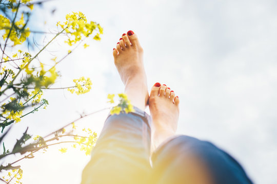 Legs up of happy female lying in deep yellow flowers meadow with bright sunny day optical sun beams flares. Happiness in nature concept POV image.