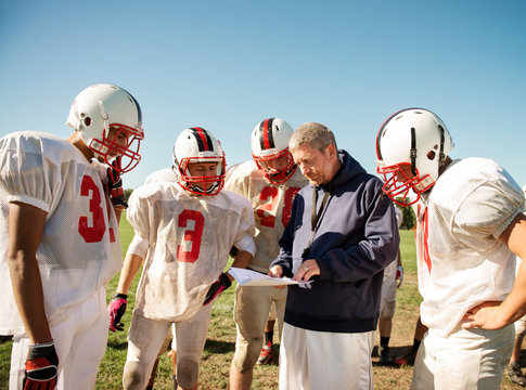 Coach instructing football players (14-15, 16-17) in field  - Powered by Adobe