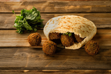 Falafel balls in a pita and green fresh parsley on a wooden background.Falafel plays an iconic role in Israeli cuisine and is widely considered to be the national dish of the country.