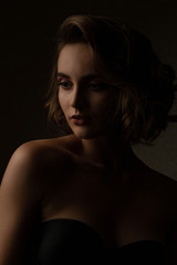 Fototapeta premium Stunning brunette model with curly hair wears lingerie posing with contrast light at studio