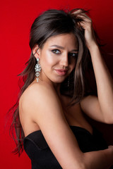 Obraz premium Charming tanned model with long shiny hair wearing earrings posing on a red background