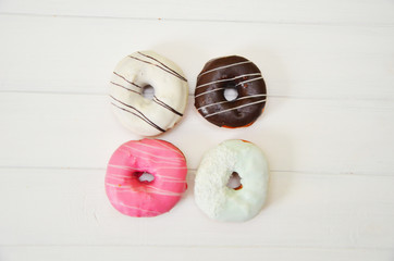 assorted donuts with chocolate frosted, pink glazed and sprinkles donuts on white wooden background