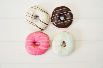 assorted donuts with chocolate frosted, pink glazed and sprinkles donuts on white wooden background