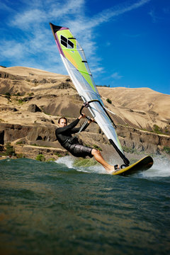 Man windsurfing in front of rocks and blue sky 