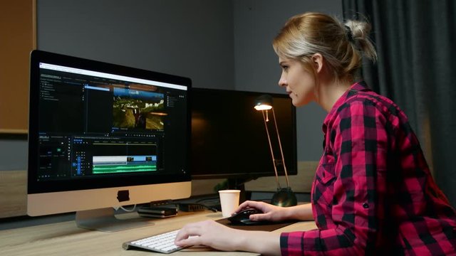Woman video editor works with footage on her computer, works in office. Video editing, side view.