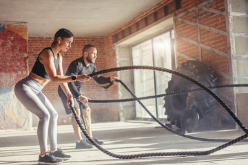 Young fitness couple in sportswear doing crossfit cardiovascular exercise using training rope at...