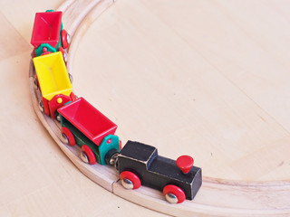 Wooden toy train running on miniature railroad tracks. The black engine pulling colorful cars on the floor. Educational toys for children in preschool and kindergarten.