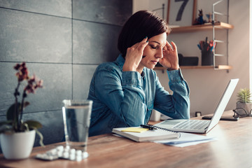 Woman with headache and capsules with glass of water on a office desk
