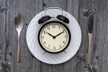 Fototapeta na wymiar Alarm clock with spoon and knife on the table. Time to eat