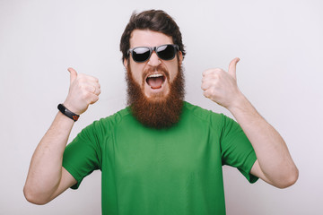 Portrait of excited happy bearded man in sunglasses, and green tshirt showing thumb up sign and...