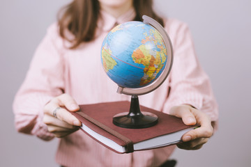 Young woman holding a brown agenda and small globus on gray background
