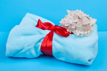 Blue fabric with a red ribbon. gift with ribbon. Shell on the fabric. Gift on a blue background