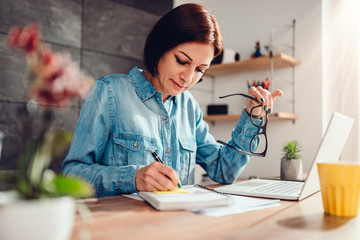 Woman writing notes in note pad and holding eyeglasses