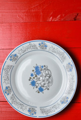 Empty white plate on red wooden background.