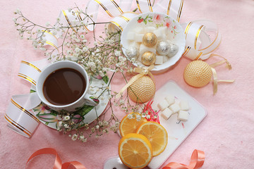 A cup of coffee with lemon and flowers in a festive ribbon, a plate with sweets on a pink background