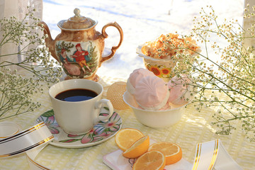 A cup of coffee and a cup of milk on the morning table near the window, dessert and spring flowers, lemon slices wishes a good day in a cozy home