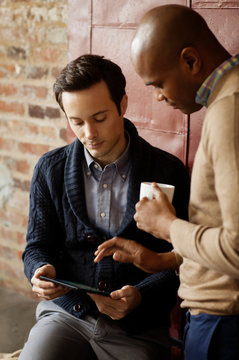 Male office workers looking at digital tablet during break,  brickwall in background  