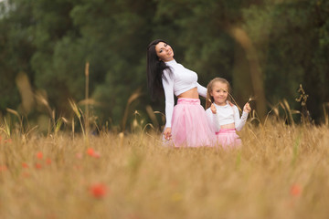 Naklejka na ściany i meble A young mother with her daughter having fun and posing in wheat fields