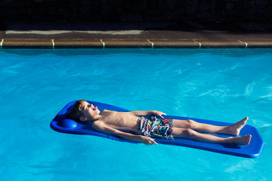Boy (10-11) floating on raft in swimming pool 