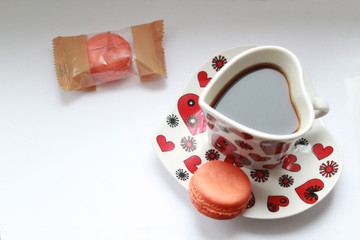 Espresso coffee in a cup in the form of heart on a saucer cake macaron, colors a coral also be near cake macaron in packing. Horizontal photo.
