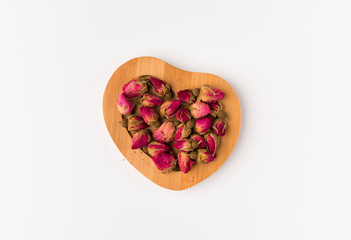 tea rose buds on a wooden saucer isolated on white background, top view