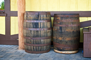 Two old antique wooden whiskey barrels or wine casks are outside against a wall.