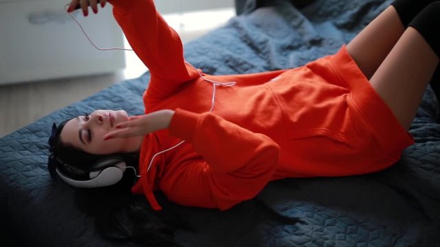 Young sexy girl talks by smartphone, online video chatting, communicate with friend lying at home bed