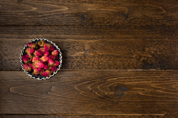 tea rose buds in a clay drinking bowl  isolated on wooden background, top view