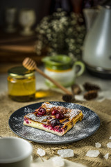 Cake with cherry clafouti on a dark plate. Klafuti with honey.