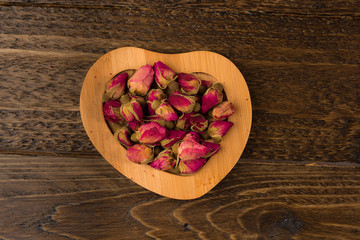 tea rose buds on the wooden saucer  isolated on wooden background, top view