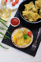 Traditional Italian homemade ravioli pasta stuffed with potatoes and spinach with tomato sauce, olive oil and basil on a black stone board