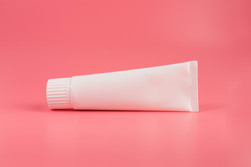 Blank white tube of toothpaste, cream or gel laying on pink background. Branding mockup