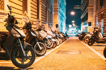 Many Motorbikes, Motorcycles Parked In City. Scooters Parked On Night Street In European City
