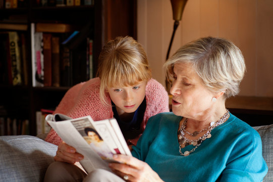 Grandmother reading newspaper to granddaughter (6-7)  